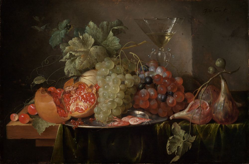 Viele bunte Früchte liegen auf einem Tisch wieTrauben, Pfirsiche, Zitronen und Beeren. In der Mitte steht ein Glas mit Wein,