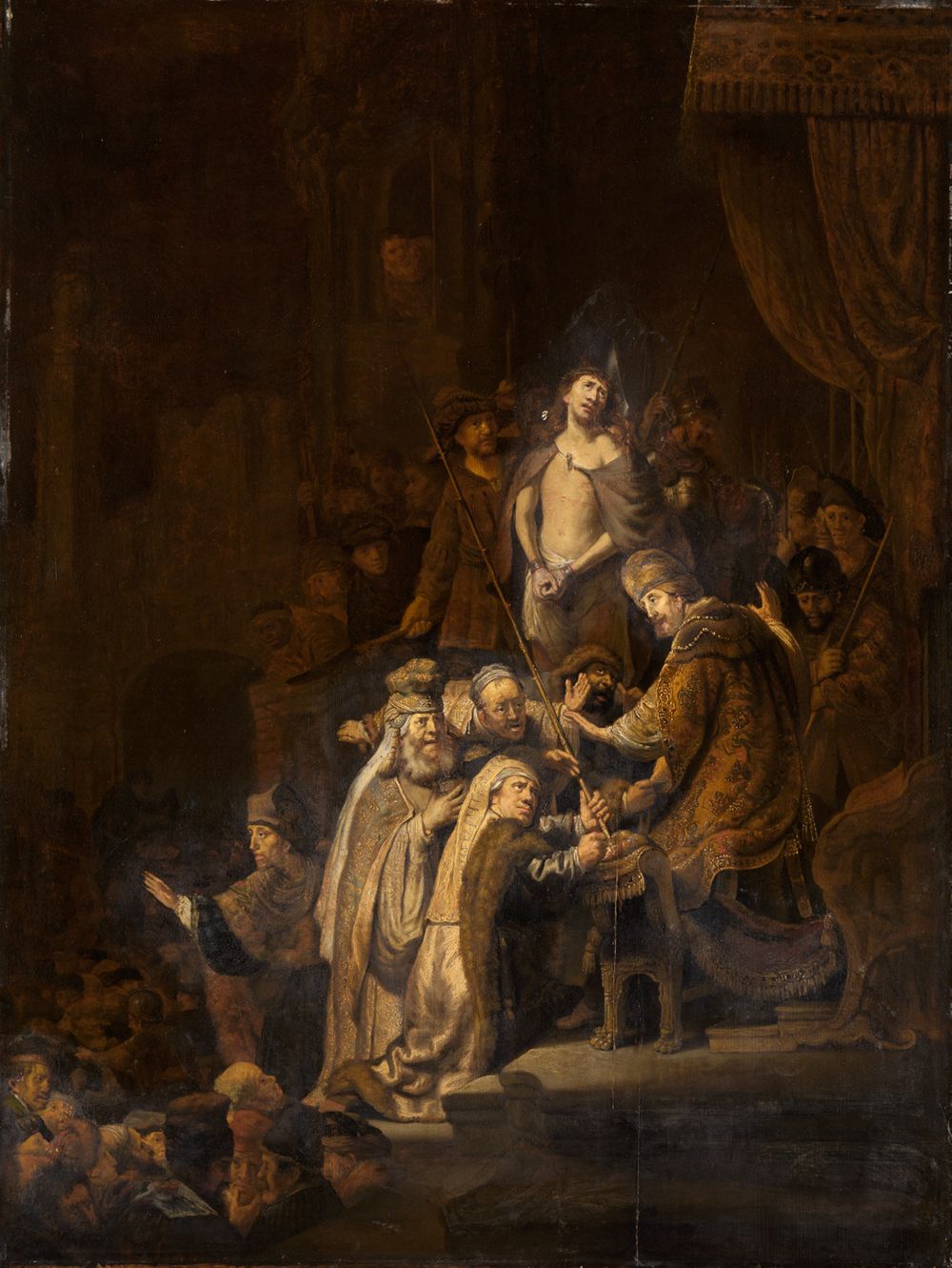 Rembrandt zeigt Jesus, der vor dem römischen Statthalter Pilatus steht, der auf seinem Thron sitzt und zu ihm hinunterschaut. Beide sind umgeben von Soldaten und weiteren Menschen.