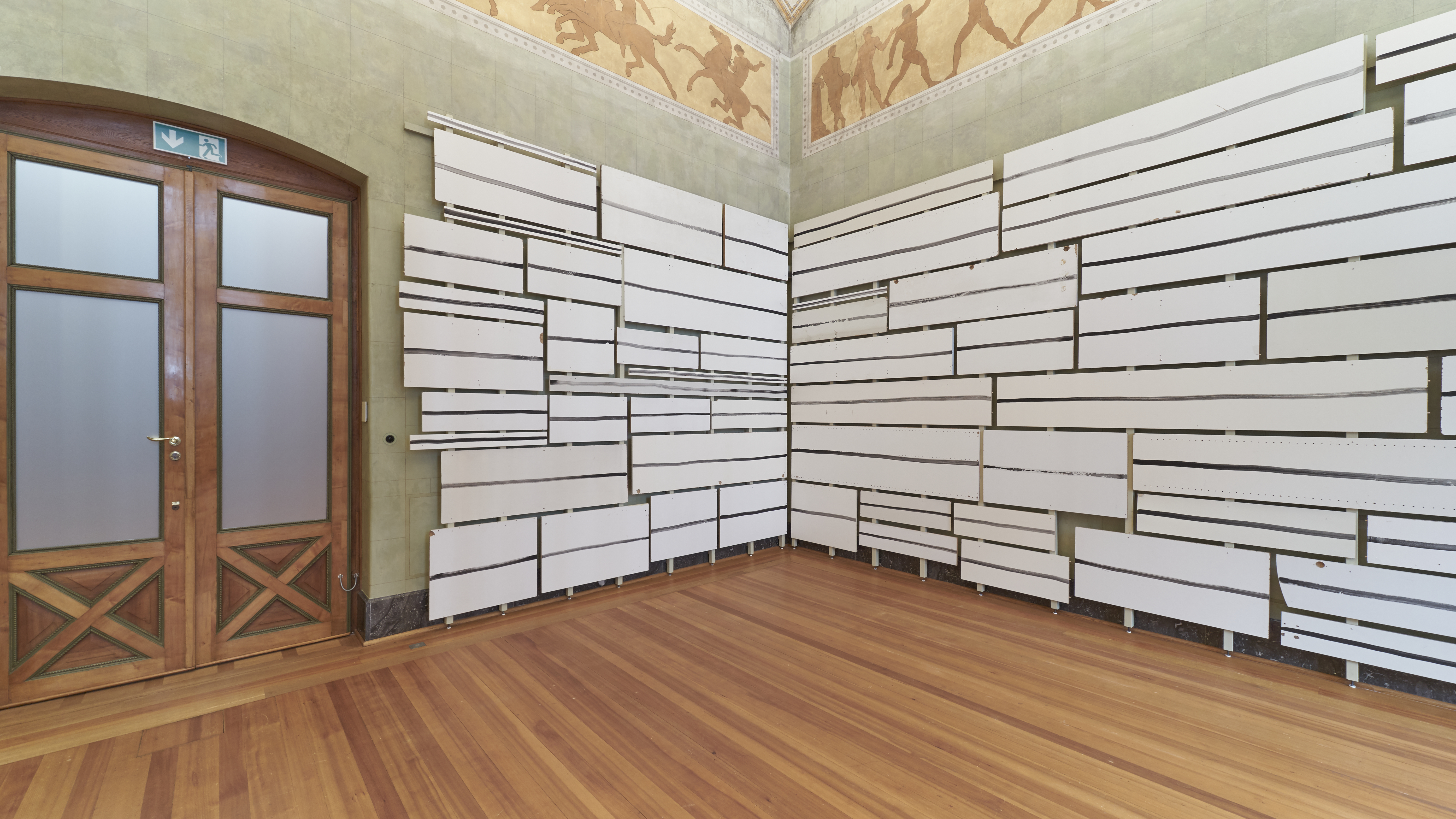 Abbildung der Rauminstallation "To have a shelf life". Sie besteht aus weißen Paneelen, die an der Wand befestigt sind.