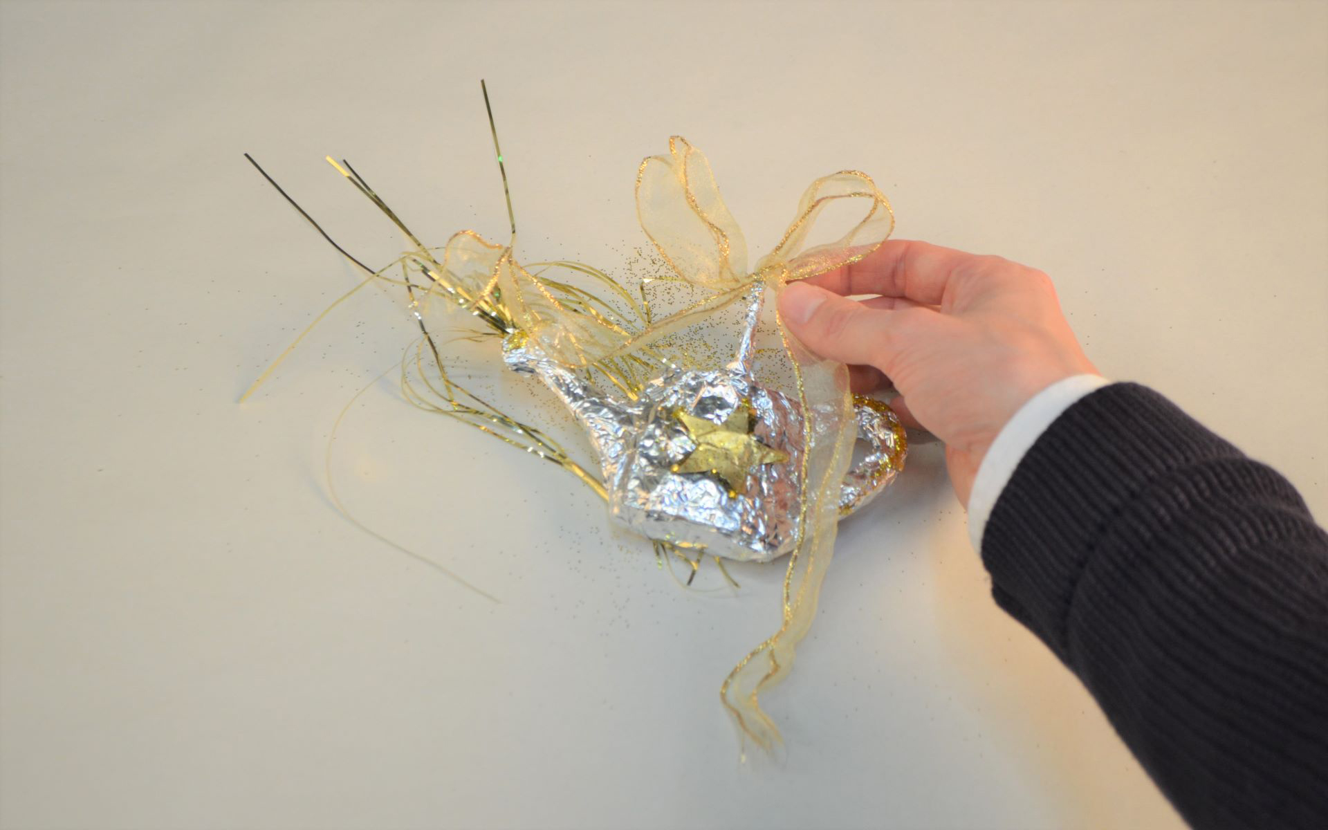 Kleine Gießkanne, die mit silberner Alufolie beklebt und mit einer Schleife aus Geschenkband versehen ist