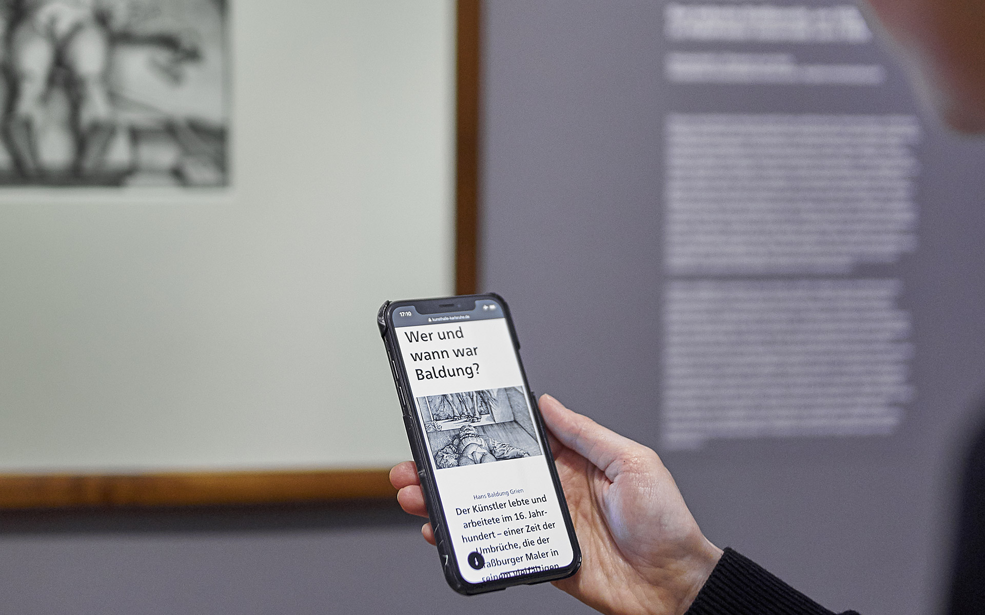 Eine Person halt ein Smartphone Hoch. DasSmartphone zeigt Webseite zur Ausstellung Hans Baldung Grien.