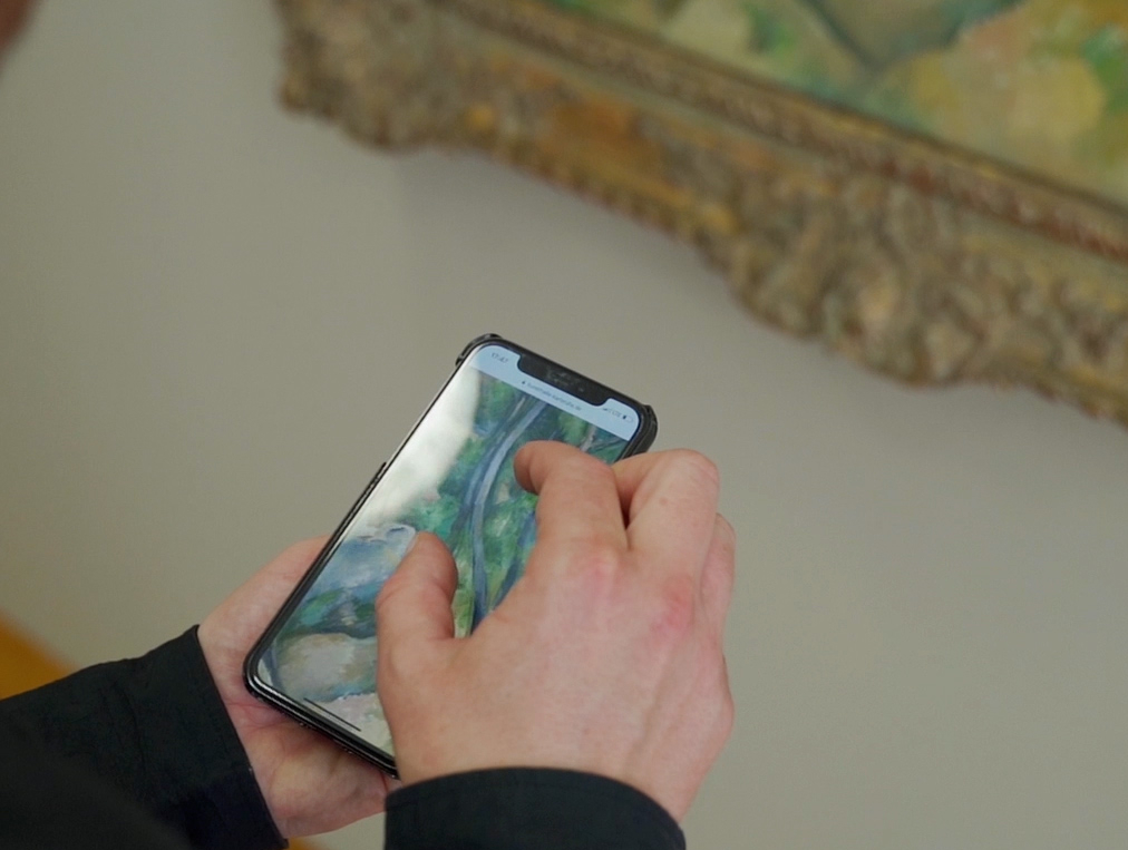 Ein Mann steht vor einem Gemälde und schaut auf das Display seines Handys.