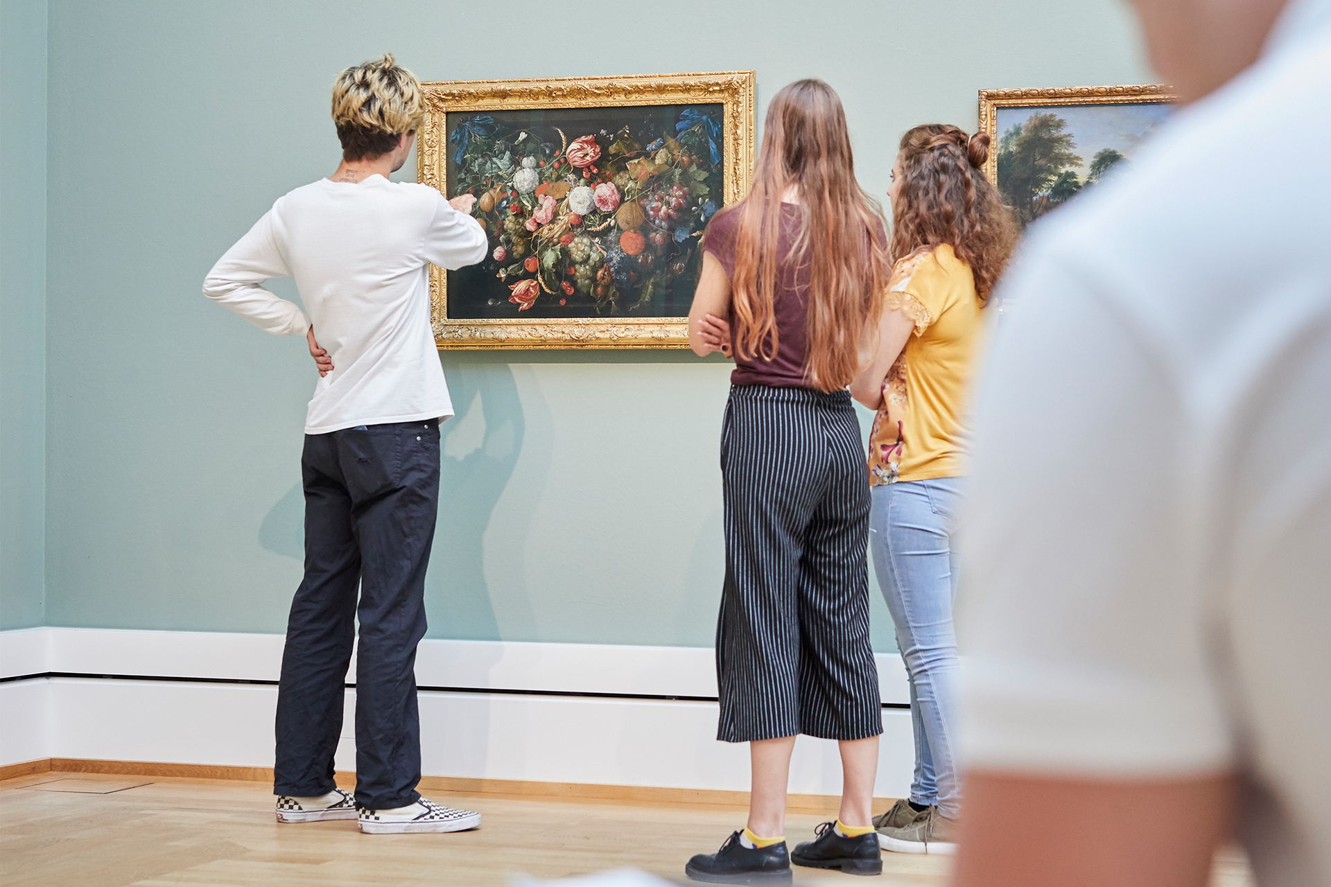 Drei junge Besucherinnen stehen vor einem Blumenstillleben und scheinen sich darüber auszutauschen. Im Vordergrund ist ein weiterer Besucher unscharf zu erkennen.