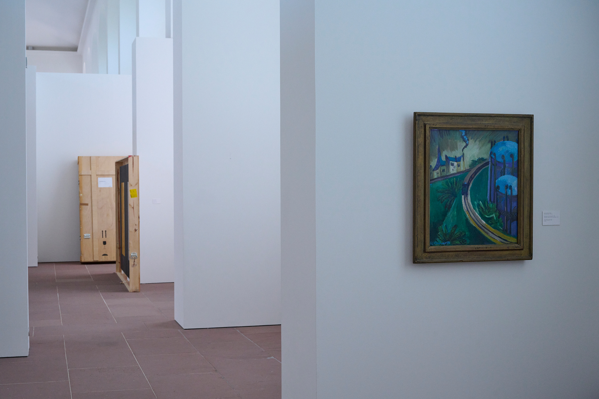 Foto von der Ausstellung in der Orangerie. Im Vordergrund ist ein Gemälde zu sehen. Im Hintergrund stehen Umzugskisten für Gemälde.