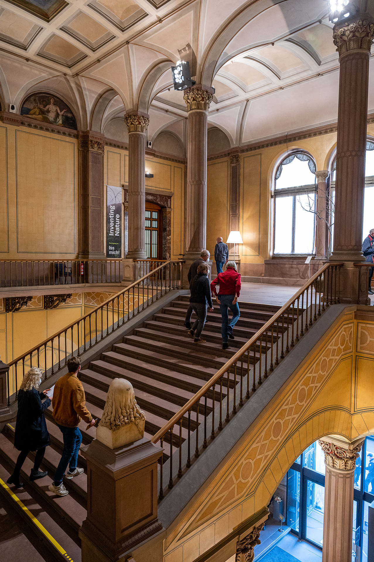 Blick auf das Treppenhaus der Kunsthalle, durch das mehrere Besucher*innnen nach oben in Richtung der Ausstellungsräume laufen.