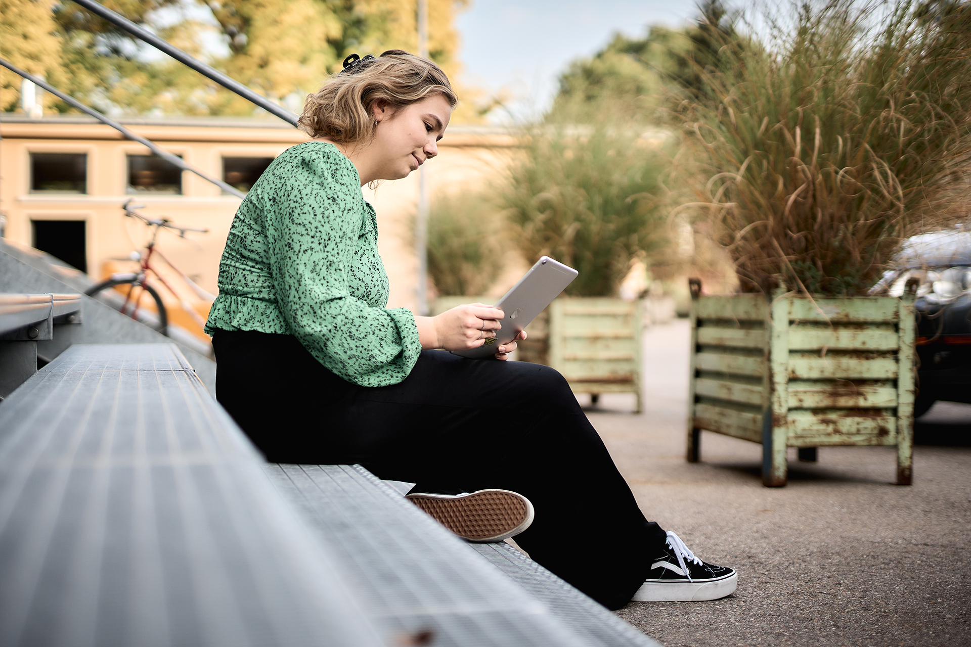 Junge Frau, die auf einer Treppe sitzt und auf einem iPad ein Kunsthallen-Angebot nutzt