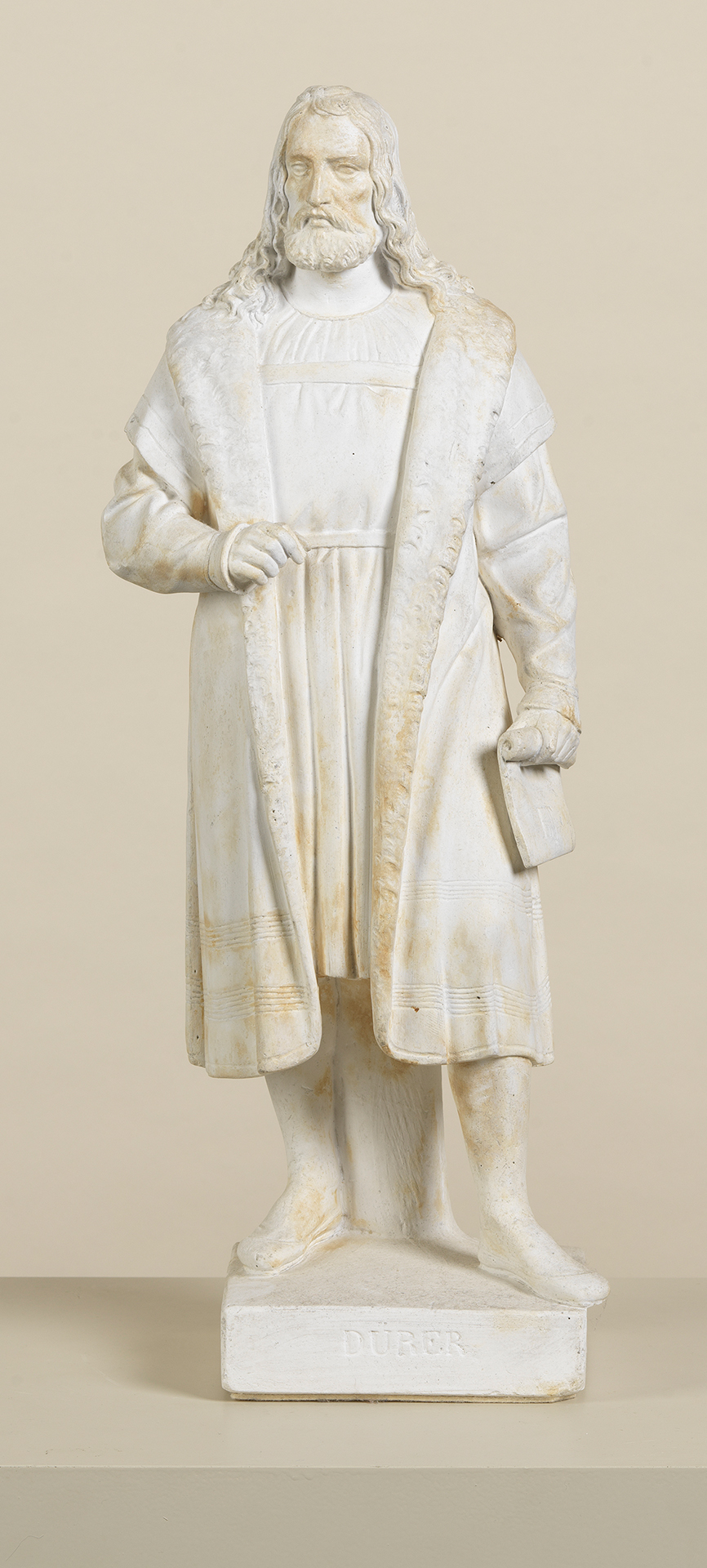Plaster cast of a small statue: Albrecht Dürer with loose curly hair wearing a long fur coat.