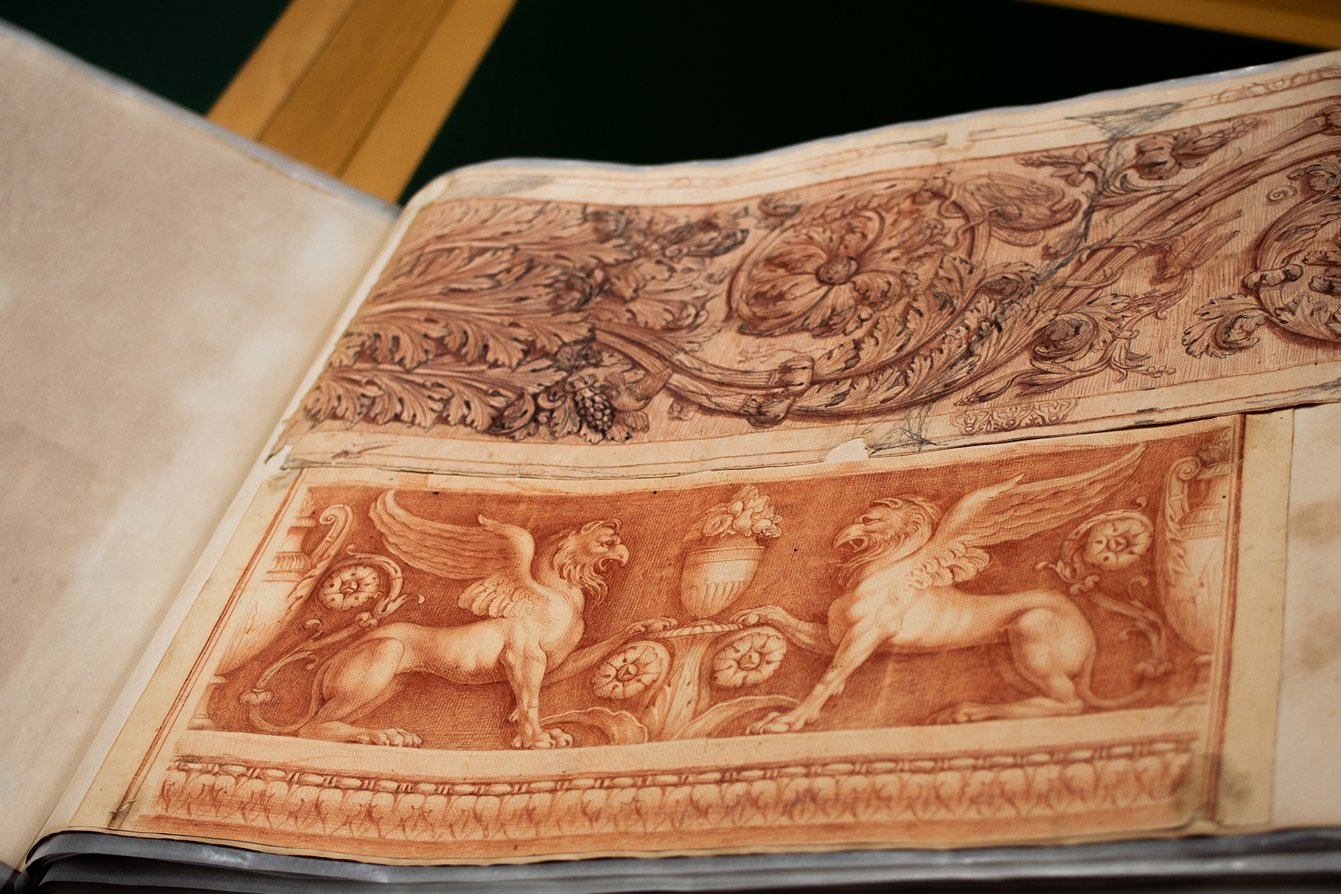 Foto des aufgeschlagenen Klebeband 1. Die aufgeschlagene Seite zeigt Blatt 10, das sowohl eine Zeichnung von zwei stolzen Greifen als auch eine Zeichnung vom Wellenrankenrelief in der Villa Medici zeigt.