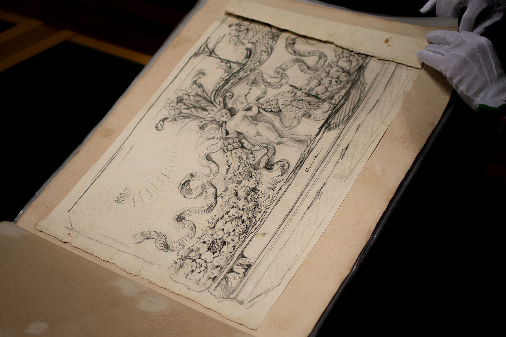 Das Foto zeigt, wie mit weißen Handschuhen in einem der Piranesi-Klebealben geblättert wird. Das Album ist aufgeschlagen und zeigt eine Zeichnung. 