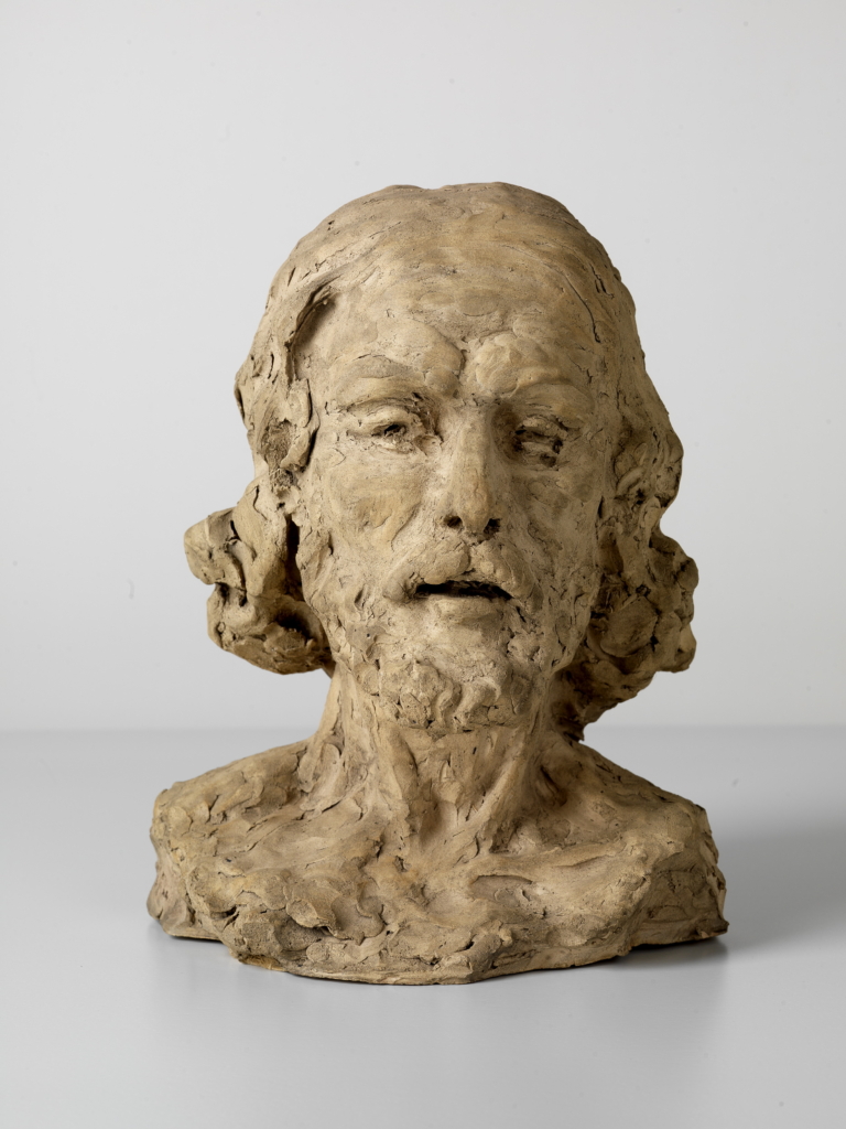 The sculpture by sculptor Auguste Rodin shows a man's head. The artwork is modeled from brown clay.