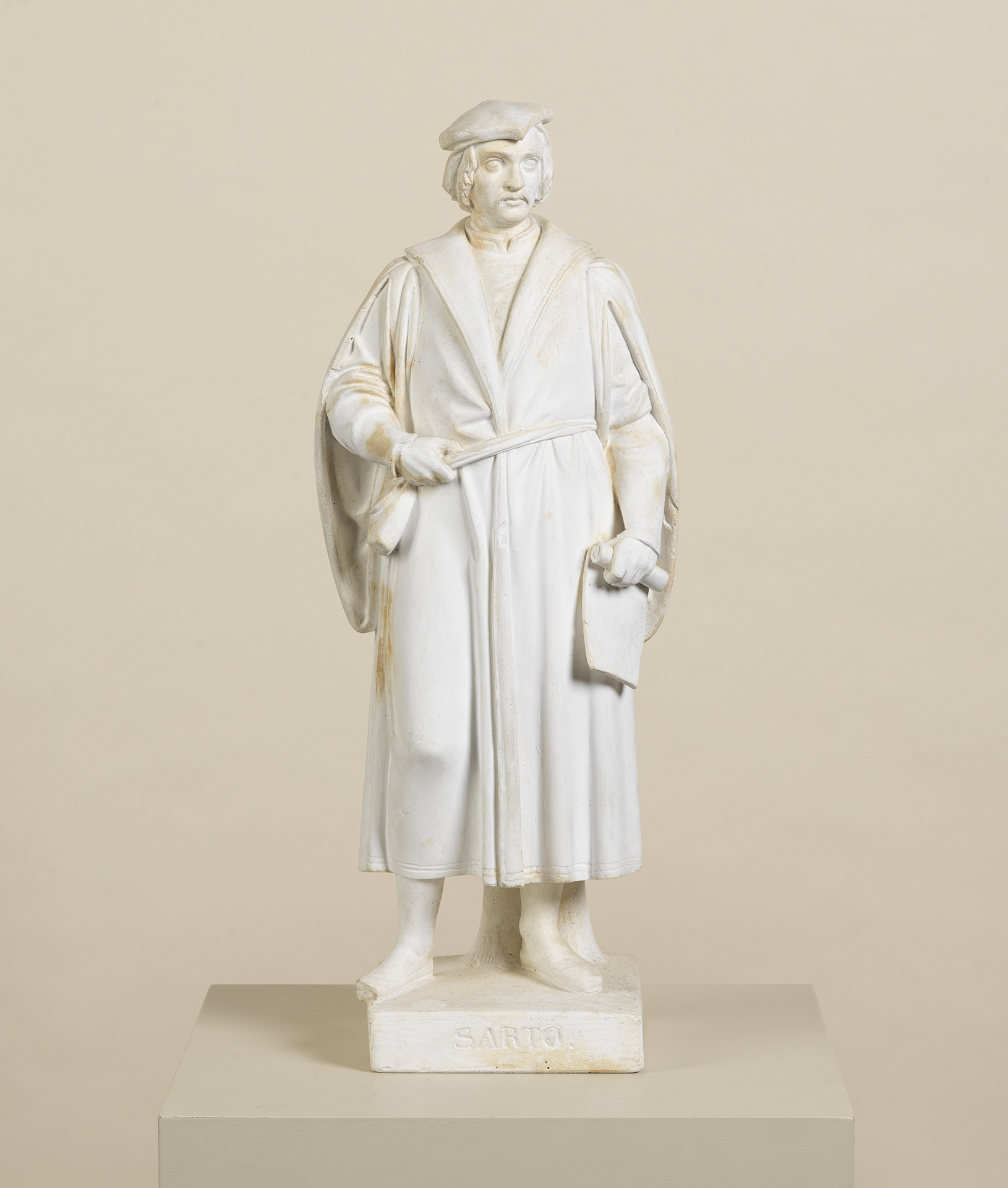 Die Skulptur zeigt den Künstler Andea del Sarto. Er trägt einen Mantel und eine Mütze. Das Kunstwerk stammt von dem Bildhauer Ludwig Schwanthaler.
