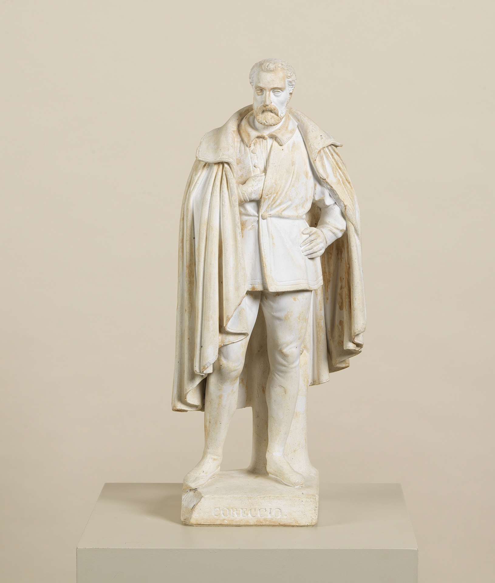 Die Skulptur des Bildhauers Ludwig Schwanthaler zeigt den Künstler Correggio. Er trägt einen Mantel und hat einen Bart. Die Skulptur ist aus weißen Gips der teils braun verfärbt ist.