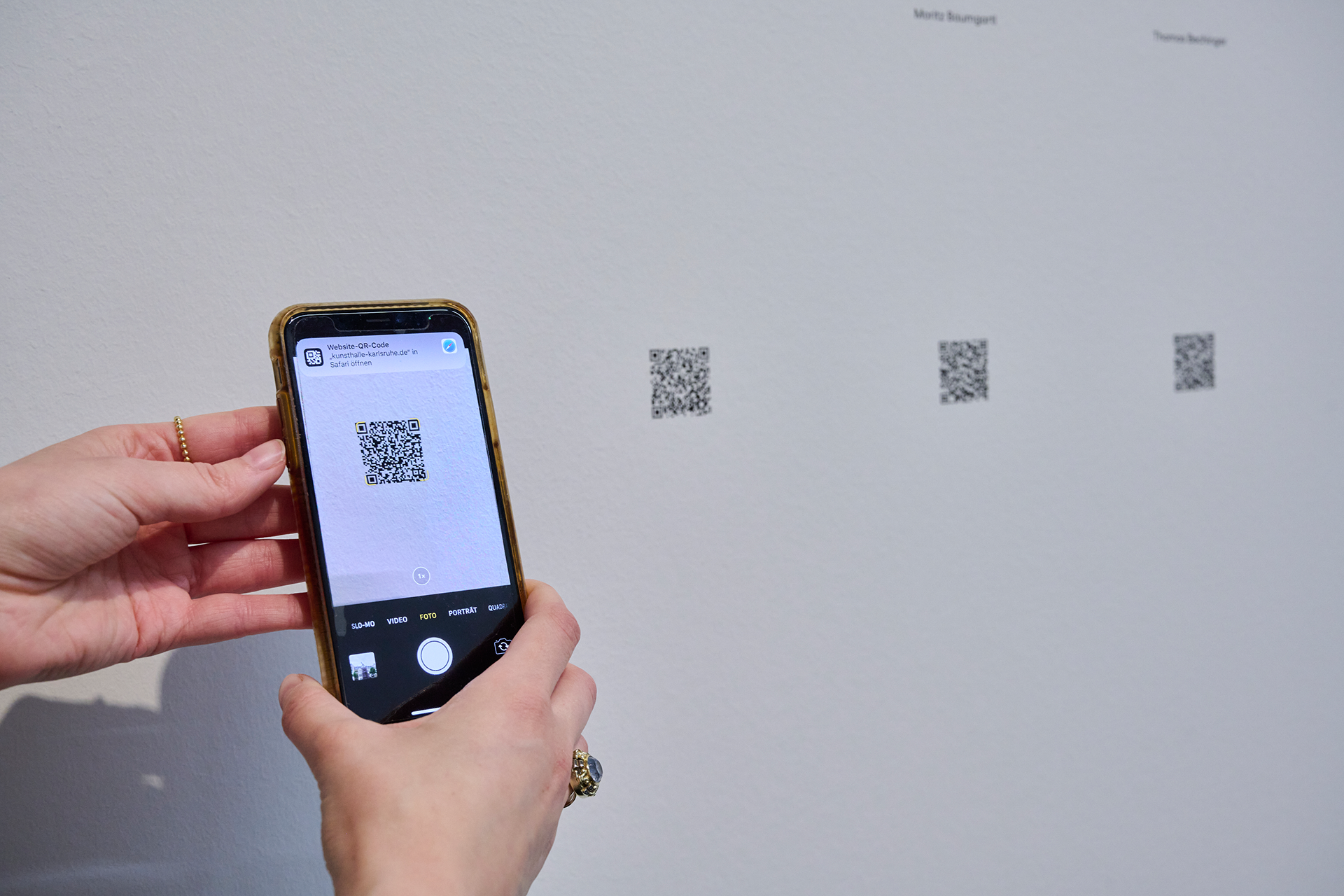 Eine Museumsbesucherin hält ein Smartphone und fotografiert einen QR-code zu einem digitalen Kunstwerk.