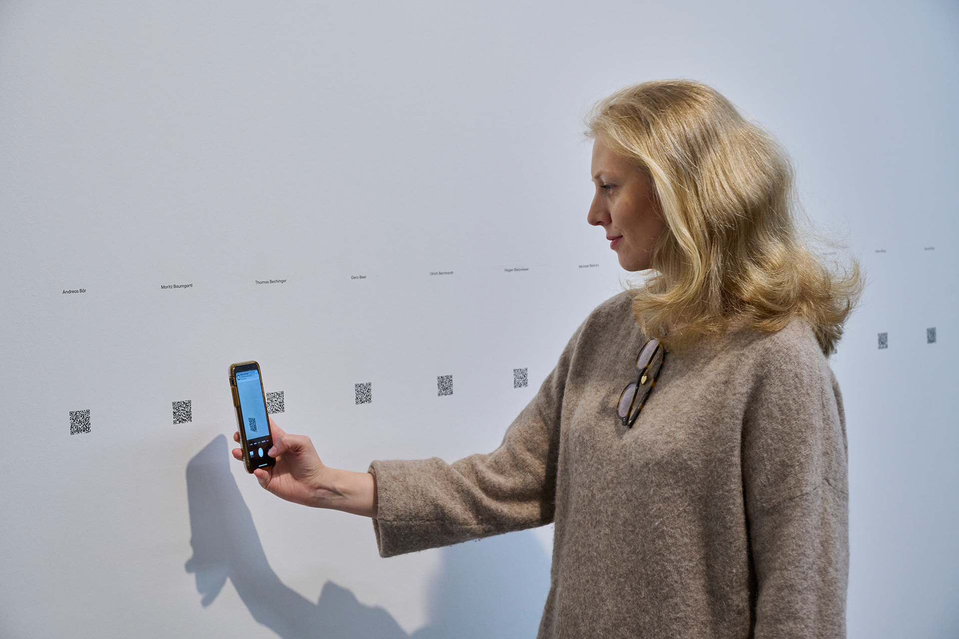 Eine hübsche blonde Museumsbesucherin fotografiert in einer Ausstellung einen QR-Code zu einem digitalen Vermittlungsguide ab.