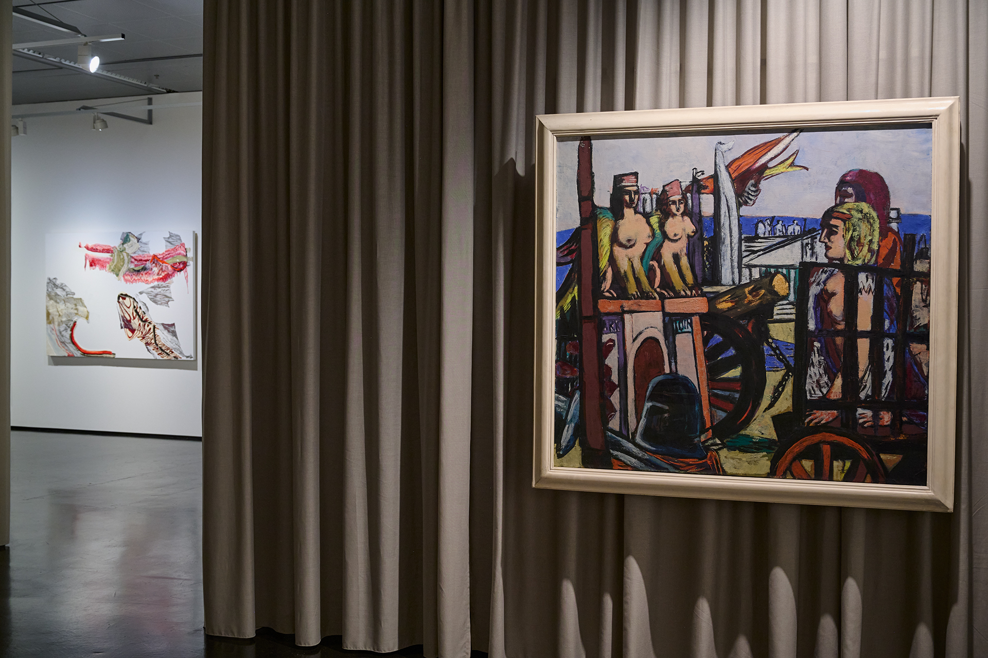 Das Foto zeigt einen Ausstellungsraum. Im Vordergrund hängt ein Bild von Max Beckmann vor einem Vorhang. Im Hintergrund kann man ein Gemälde von Pia Fries erkennen.