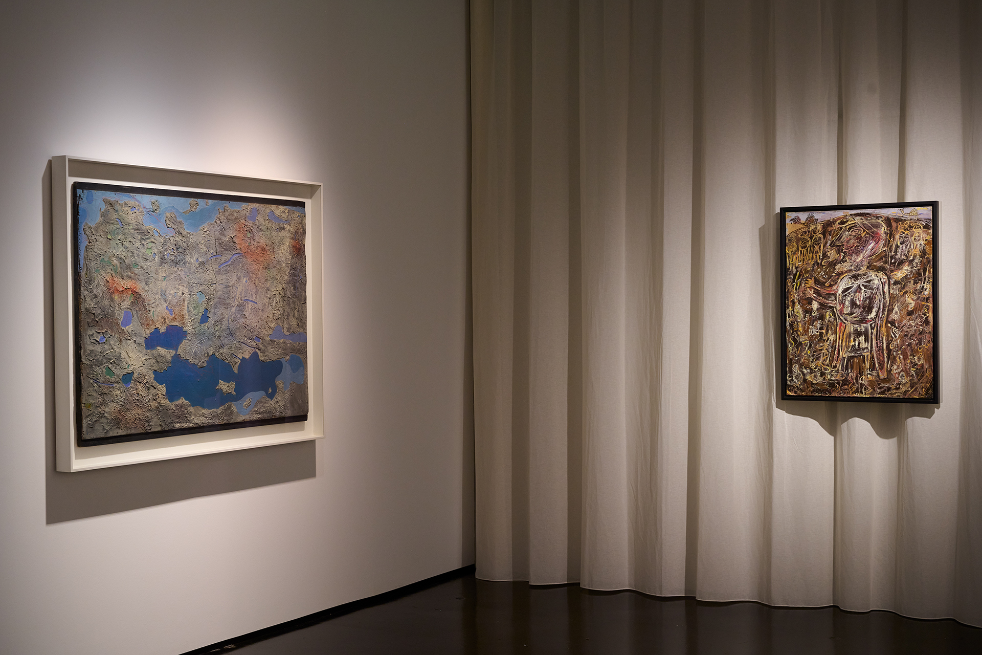 Das Foto zeigt einen Ausstellungsraum mit zwei Gemälden. Eines davon, hängt an einem Vorhang.