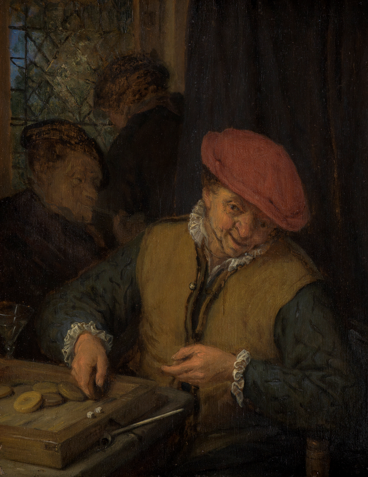 Ein Mann sitzt an einem Tisch, auf dem ein Brettspiel mit Würfeln steht. Im Hintergrund des engen Zimmers zwei weitere Personen im Dunkeln.