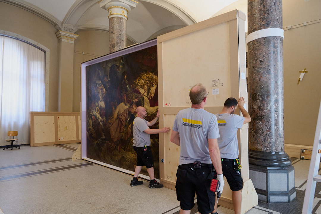 Auf dem Foto sieht man, wie ein großes Gemälde der Kunsthalle Karlsruhe gerade in eine Kiste verpackt wird.