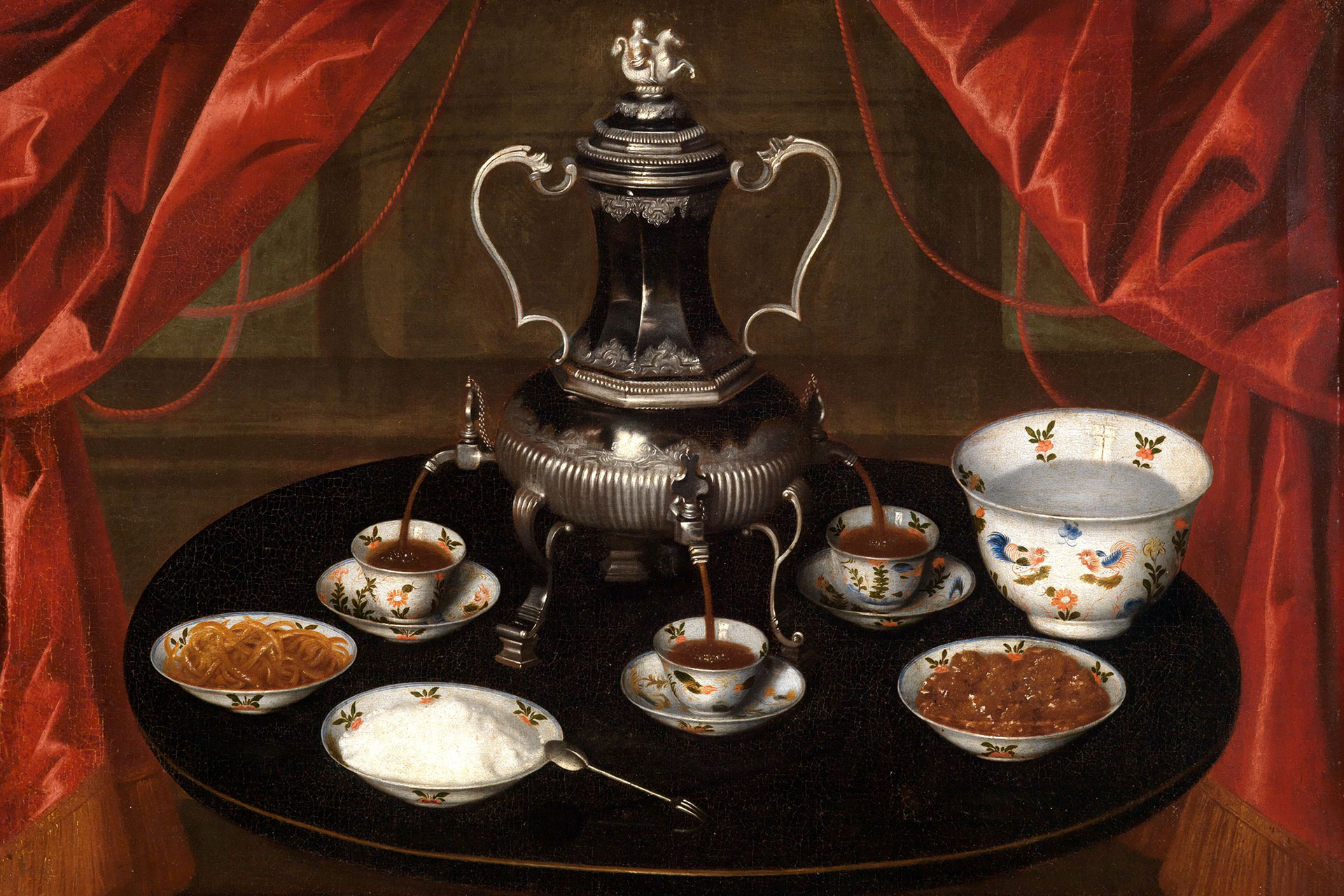 Kaffeetafel eines Deutschen Meisters. Zu sehen ist ein runder Tisch mit einem Samovar in der Mitte. Unter ihm stehen drei Tassen in die Kaffee hineinläuft. Auf dem Tisch stehen weitere Schalen mit Lebensmitteln. Im Hintergrund ist ein roter Vorhang.