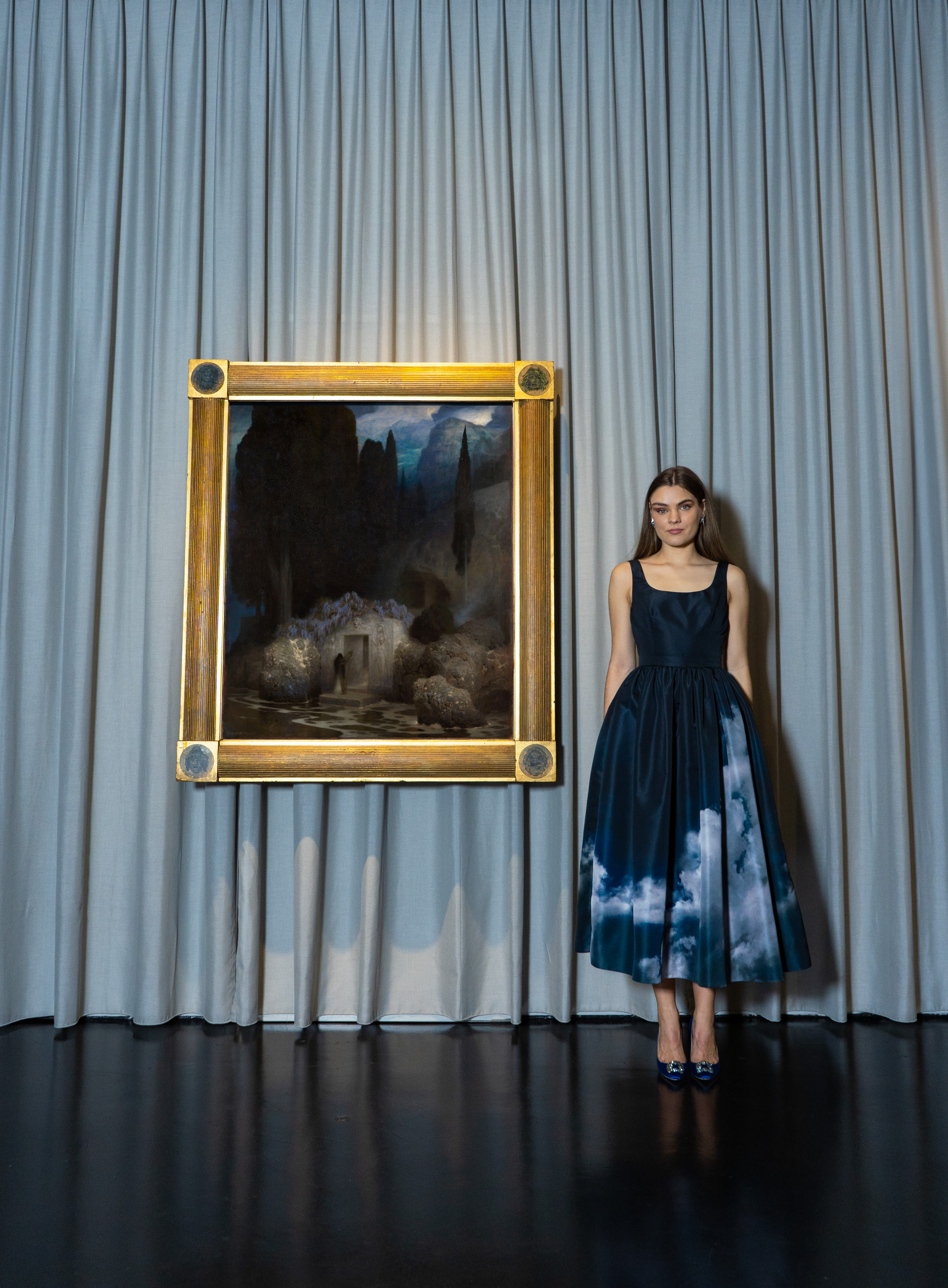 Eine Frau in einem langen dunkelblauen Kleid mit Wolken darauf neben dem Kunstwerk von Friedrich Keller.