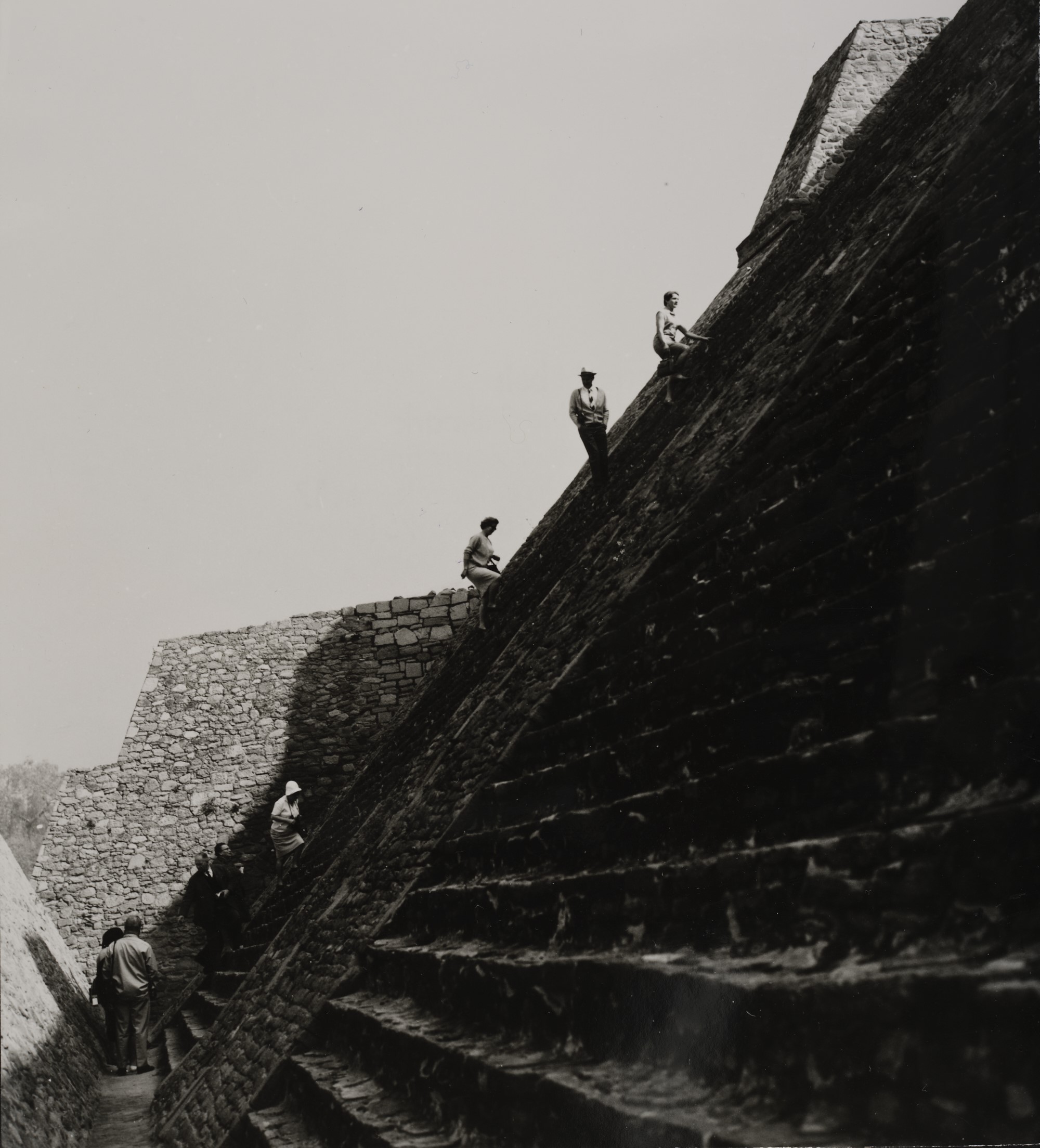 Die Fotografie zeigt Personen, die eine Pyramidenarchitektur hinaufsteigen.