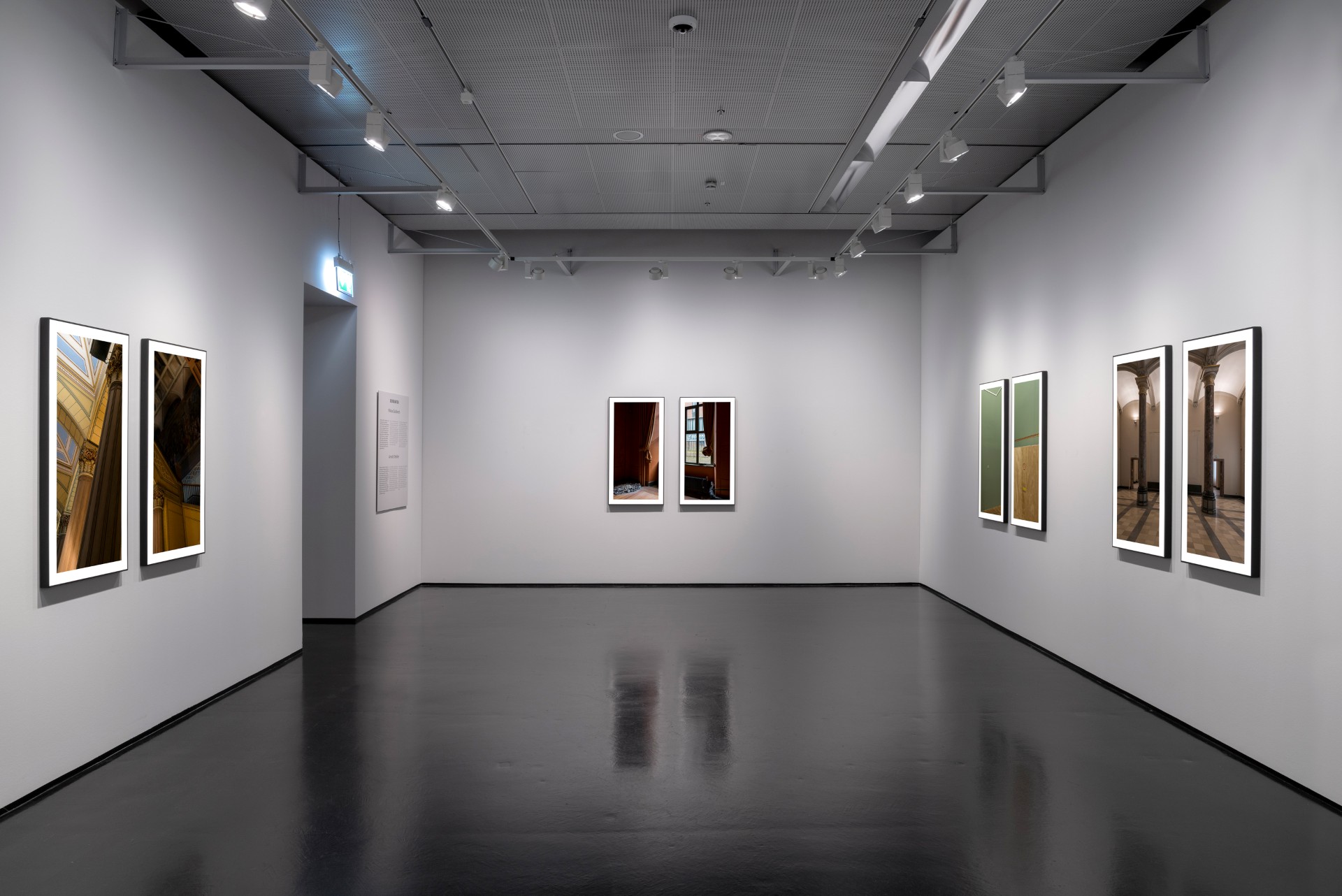 Blick in die Ausstellung Drift mit großformatigen Fotoarbeiten, die paarweise in schwarzen Rahmen an grauen Wänden hängen und die leeren Innenräume des historischen Gebäudes der Kunsthalle zeigen.