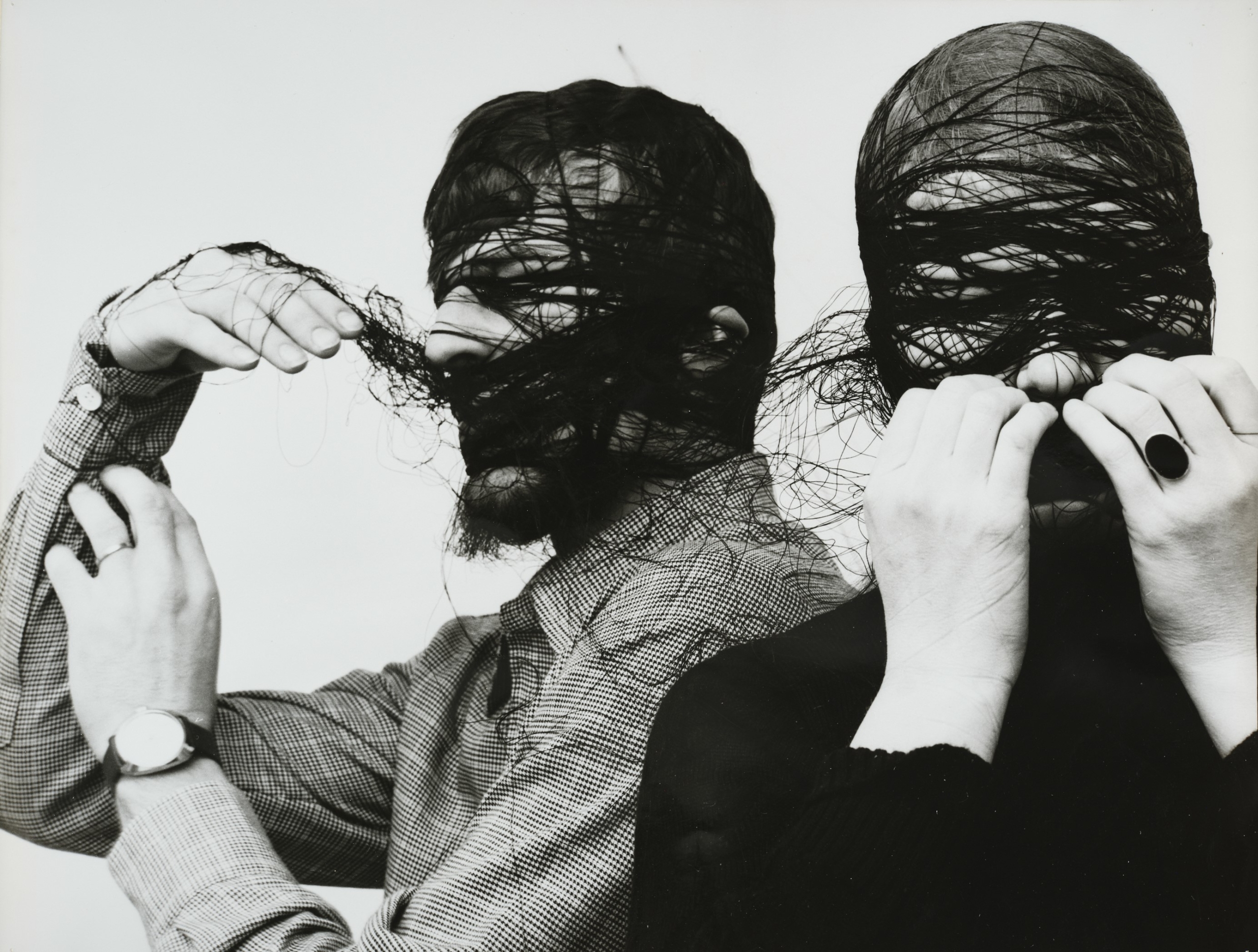 Zwei Männer sind in einer schwarzweiß Fotografie abgebildet. ihre Gesichter sind mit Faden umwickelt und wirken daher deformieret. Mit ihren Händen versuchen sie sich davon zu befreien.