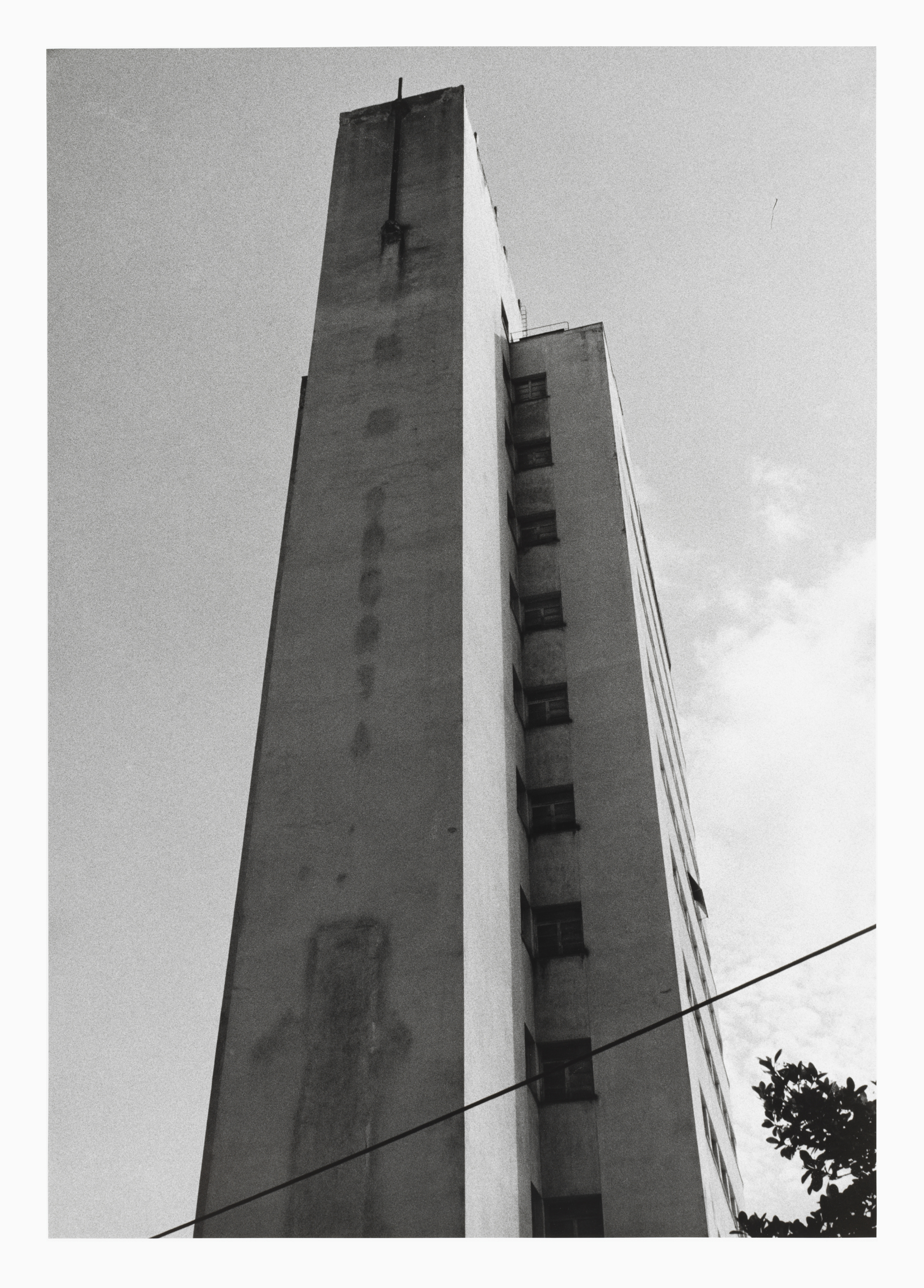 Ein Hochaus ist in von unten nach oben fotografiert. Es sieht gigantisch aus und ragt in den fast wolkenlosen Himmel. Wir sehen eine Seite des Gebäudes mit wenigen Fenstern.