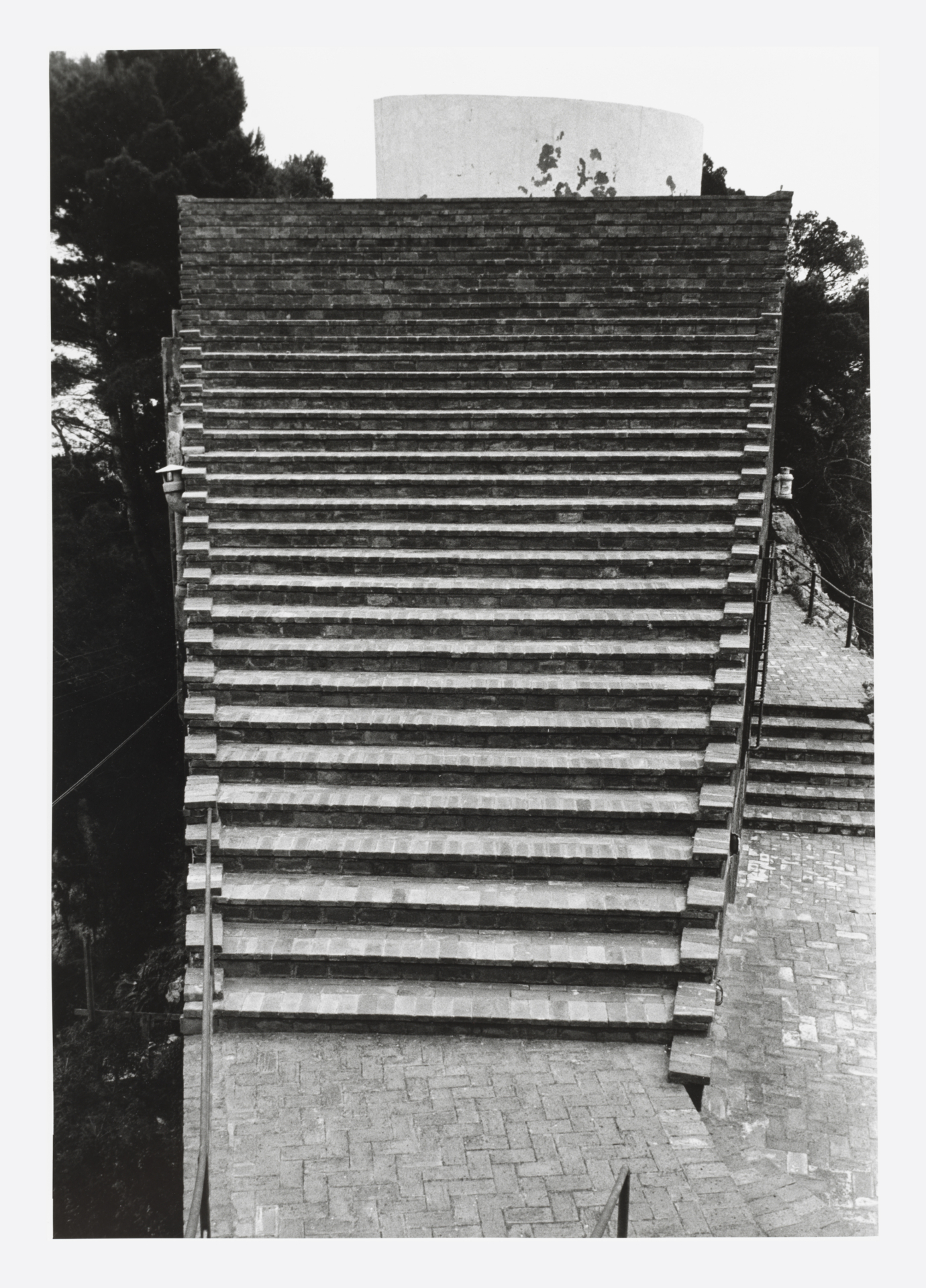 Die breite Treppe, die fast das ganze Bild einnimmt, führt auf der Dachterrasse der Villa Malaparte. Auf der linken Seite stehen Bäume.