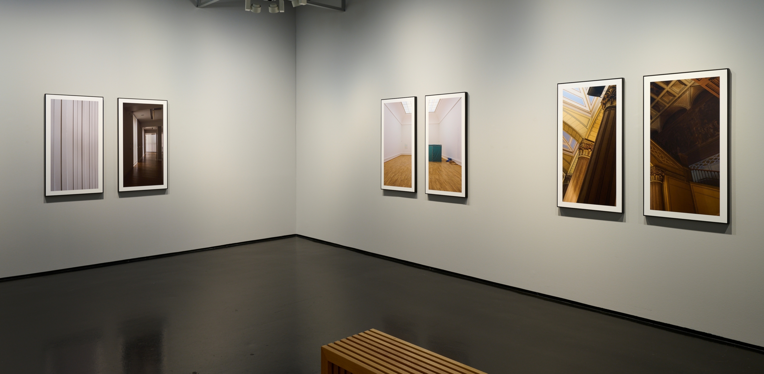 Blick in die Ausstellung Drift mit großformatigen Fotoarbeiten, die paarweise in schwarzen Rahmen an grauen Wänden hängen und die leeren Innenräume des historischen Gebäudes der Kunsthalle zeigen.