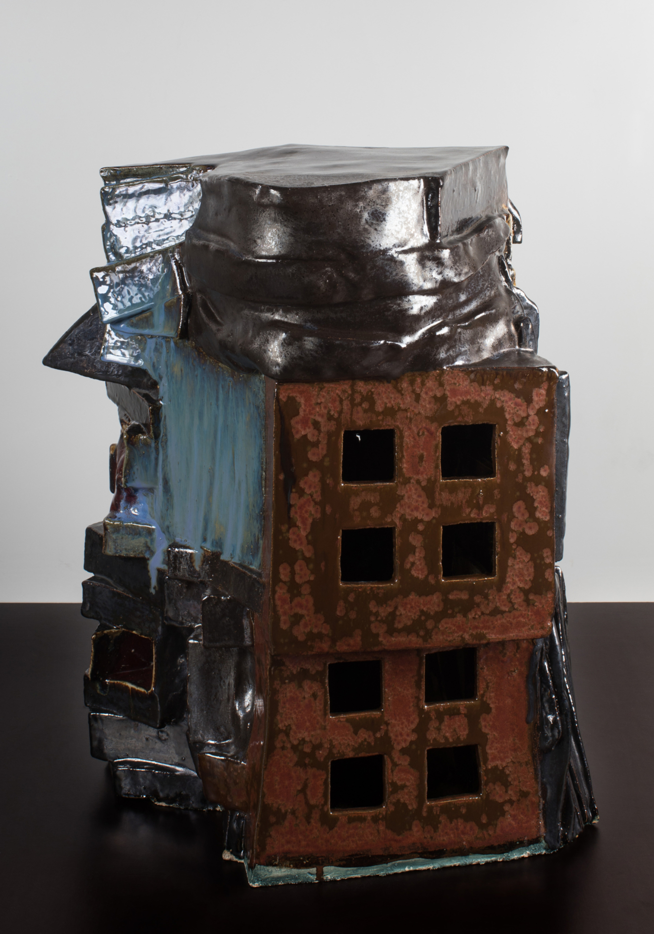 Eine ca. 50 cm hohe Skulptur steht auf dem Boden. Sie besteht aus unterschiedlichen zusammengesetzten Formen. Ihre Oberfläche ist teilweise glatt oder rau.