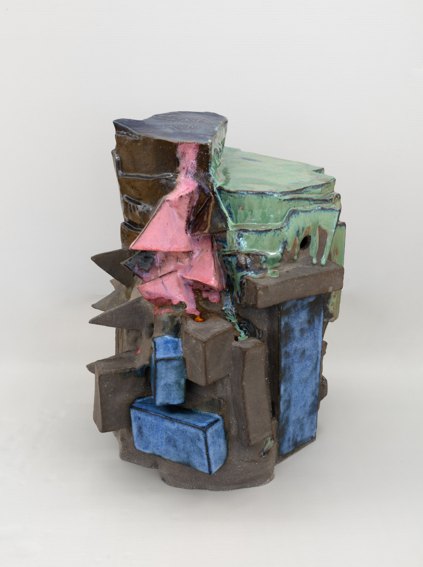 Eine ca. 50 cm hohe Skulptur steht auf dem Boden. Sie besteht aus unterschiedlichen zusammengesetzten Formen. Ihre Oberfläche ist teilweise glatt oder rau.