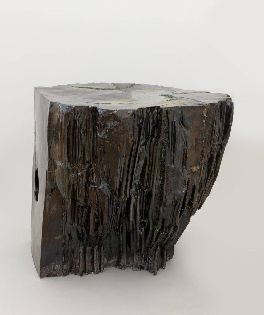 Eine ca. 50 cm hohe Skulptur steht auf dem Boden. Sie besteht aus unterschiedlichen zusammengesetzten Formen. Ihre Oberfläche ist teilweise glatt oder rau.