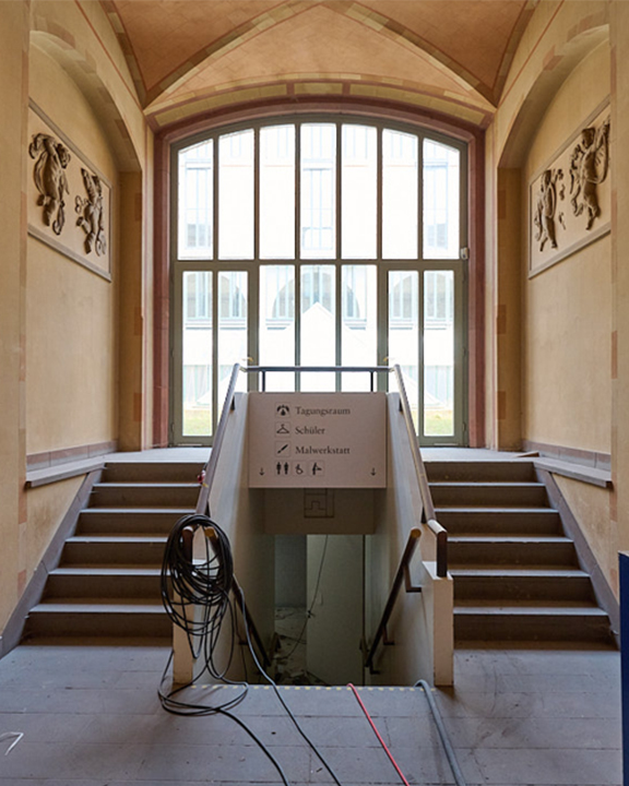 Blick ins derzeitige Foyer des Hauptgebäudes der Kunsthalle eine Treppe in der Mitte führt nach unten und zwei Treppen links und rechts daneben führen nach oben in den offenen Lichthof dahinter. Aus dem Untergeschoss führen Kabel nach oben durch den Raum.