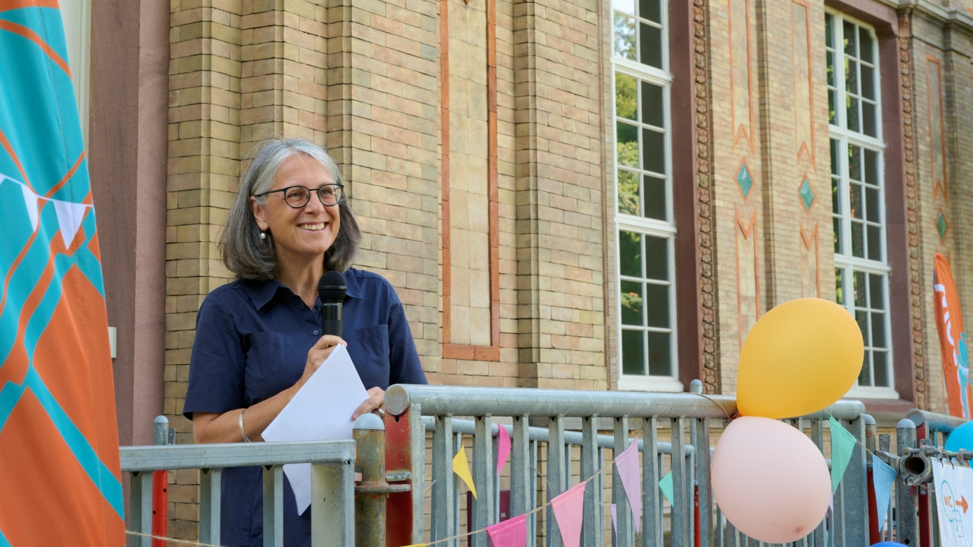 Sylvia Jung ist auf einer Bühne an einem Mikrofon vor der Orangerie zu sehen.