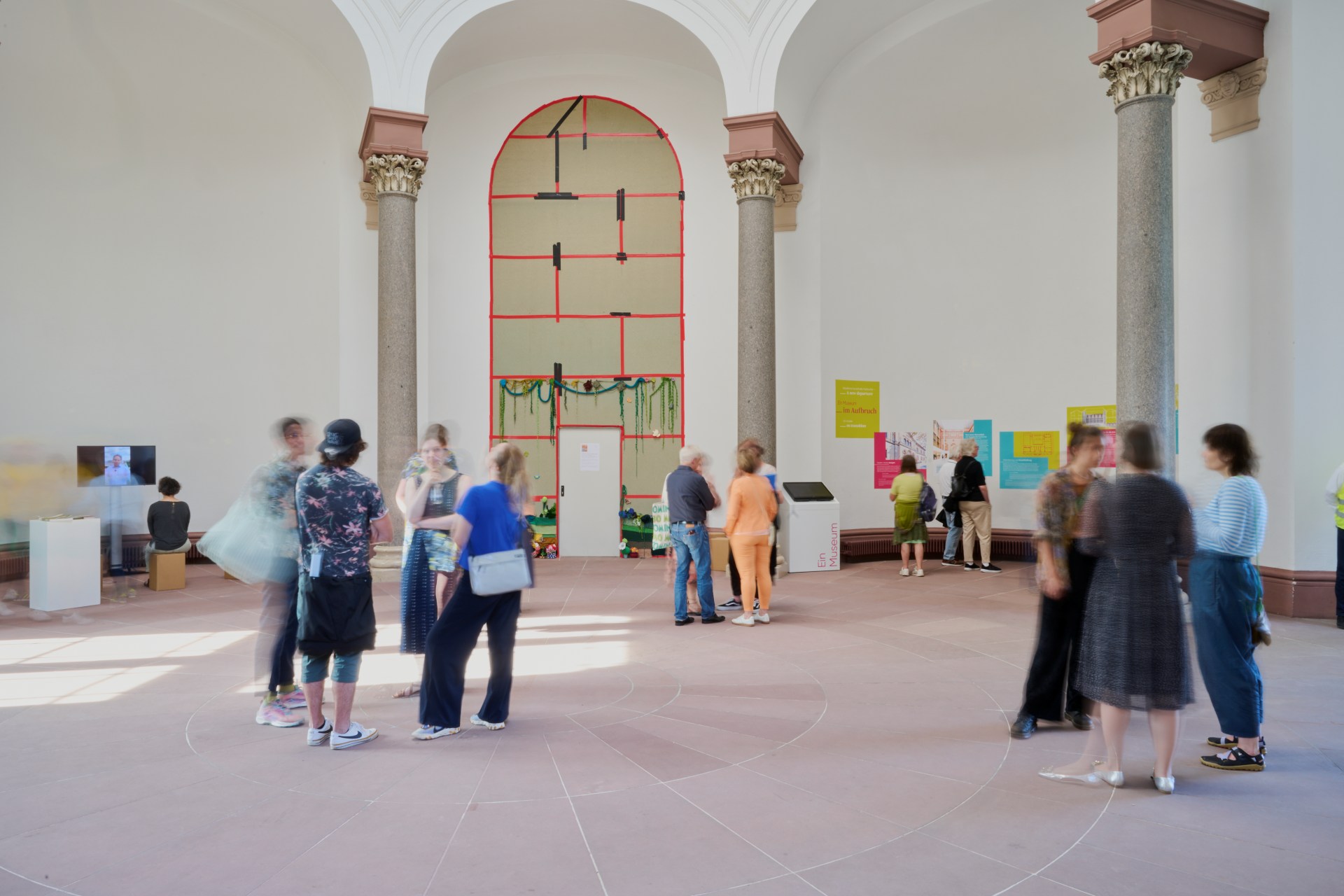 Blick in die Rotunde der Orangerie. Ein Raum mit rundem Grundriss und Säulen. Personen stehen in Grüppchen zusammen und unterhalten sich.